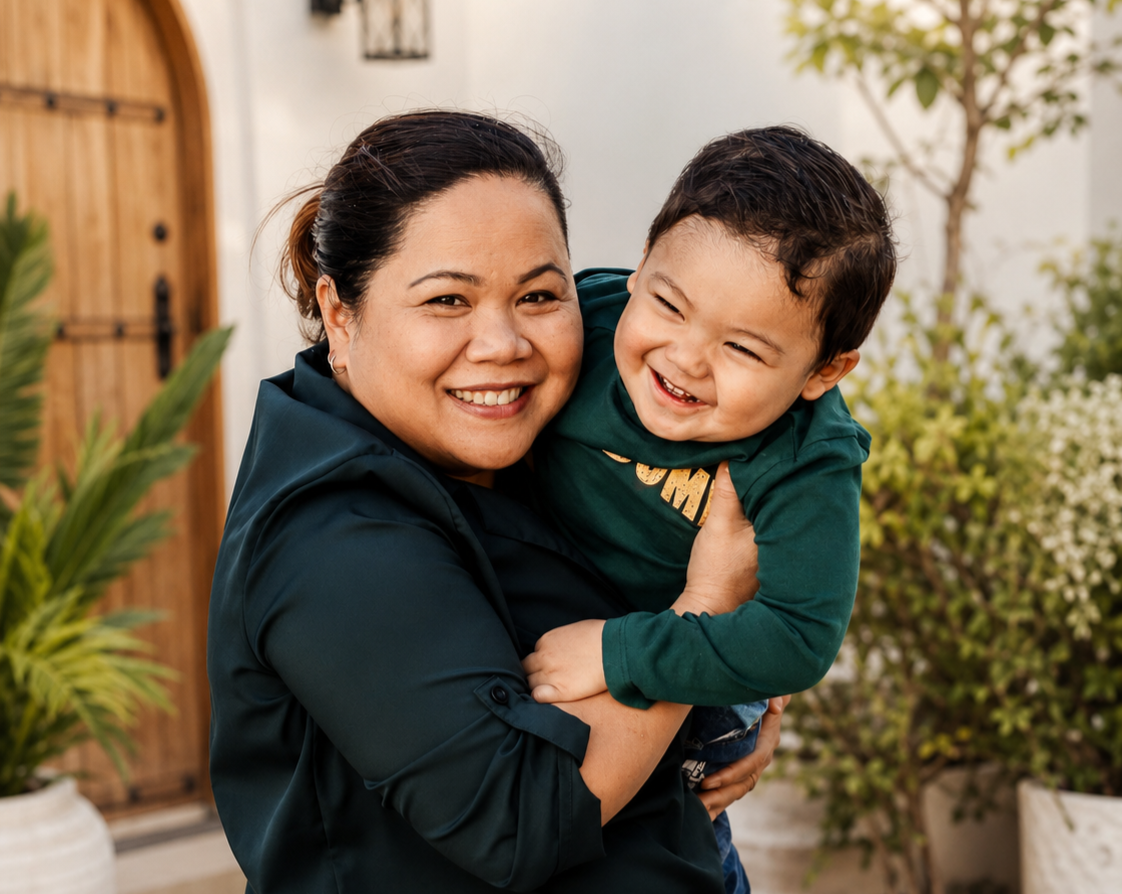 Lydia Michael with her son, smiling outside a sunny home entrance